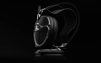 Close-up of black over-ear headphones with a chrome grille and cushioned ear cups on a dark background.