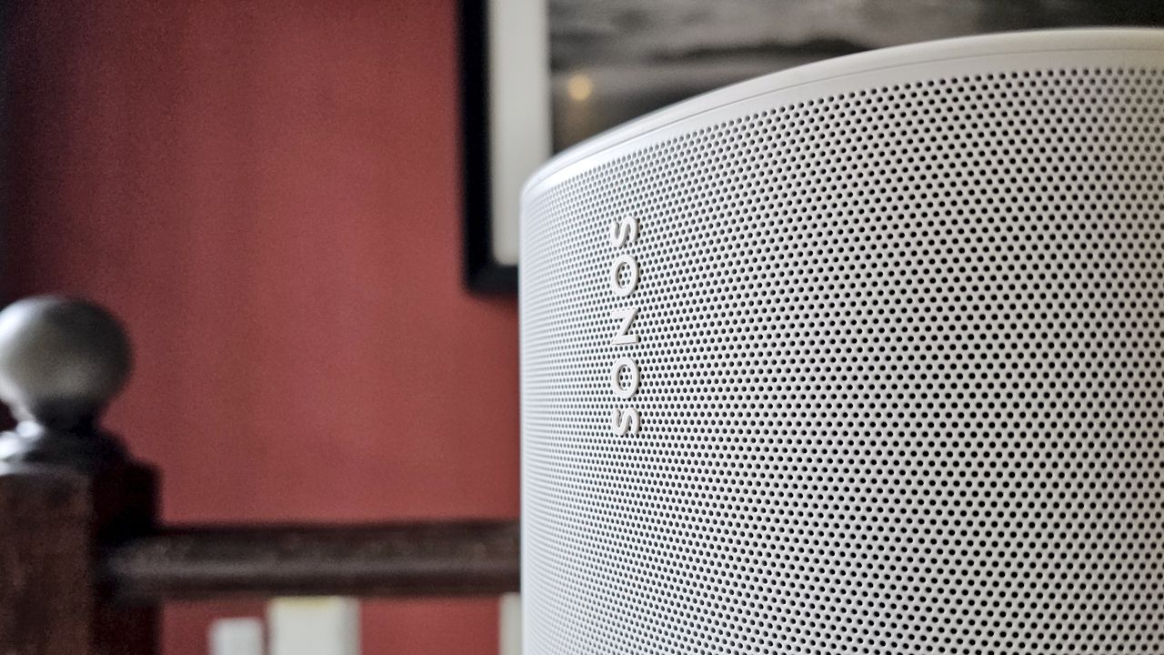 Close-up of a silver Sonos speaker grille with the brand name visible, set against a red wall and wooden railing.