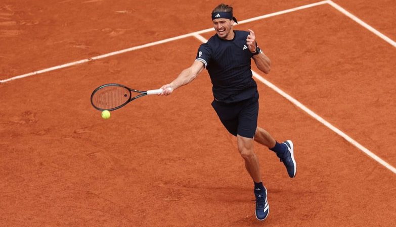 Male tennis player in a black outfit on a red clay court extends a forehand, racket reaching for a bright yellow ball just ahead of him on the court lines.