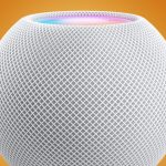 Close-up of a white spherical mesh smart speaker on an orange background with a subtle blue ring at the top edge.